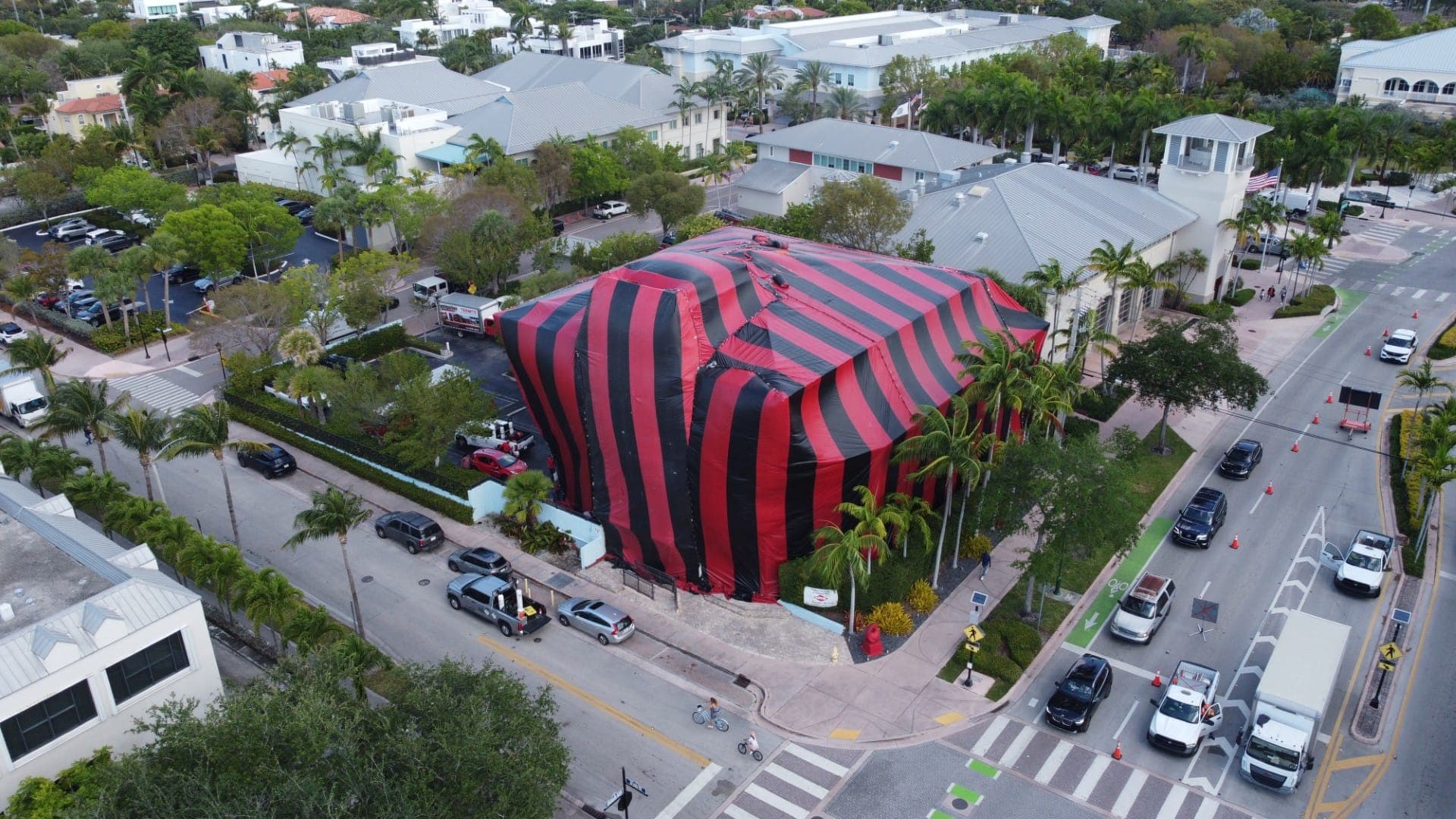 Aerial photo of a large building tented for fumigation at a busy downtown Miami intersection, with a KJC Fumigation box truck parked at the curb.