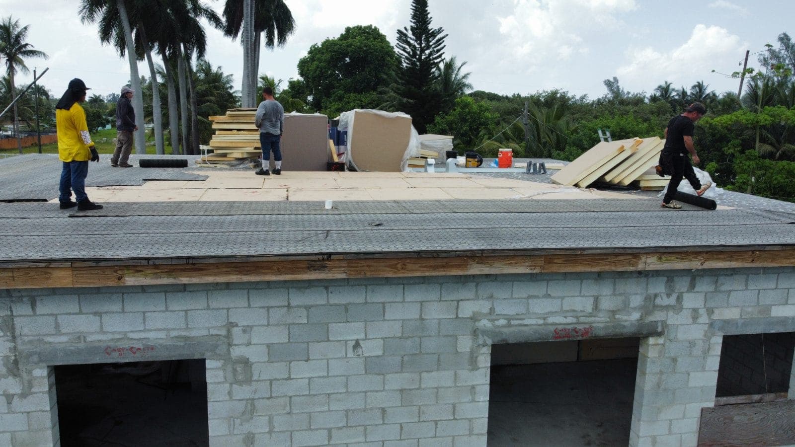 Aerial photo of three Stable Rock Construction roofers laying insulation board on a flat roof in a South Florida canal neighborhood.